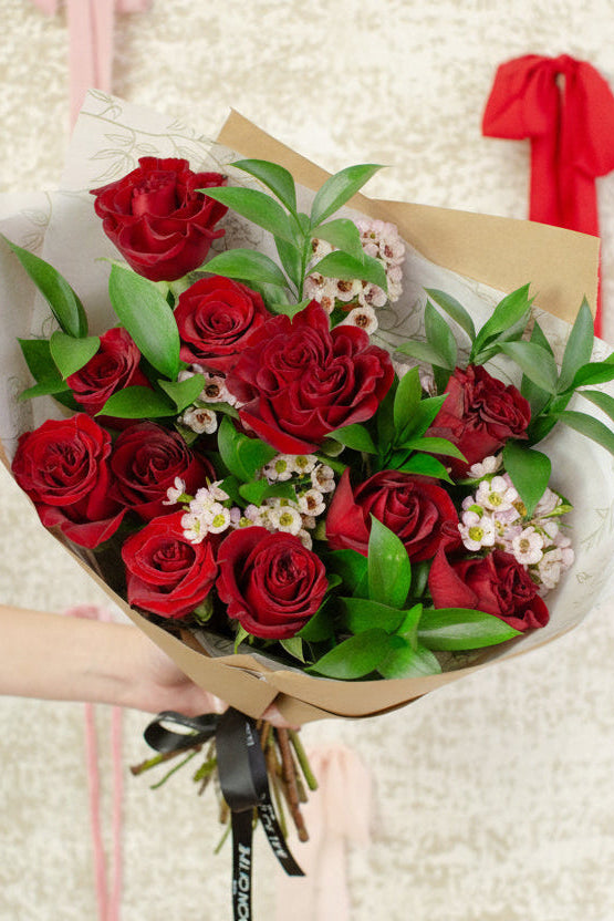 Bouquet of red roses held by a hand on a textured beige background with ribbons.
